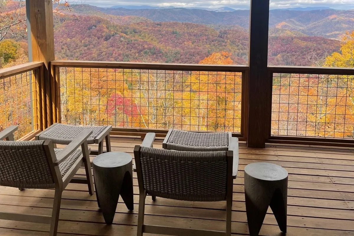 A wide outdoor seating area surrounded by vibrant autumn foliage, facing a sweeping mountain view. Cozy chairs invite relaxation, and the space feels open to the natural landscape, ideal for soaking up the scenery or joining in outdoor activities.
