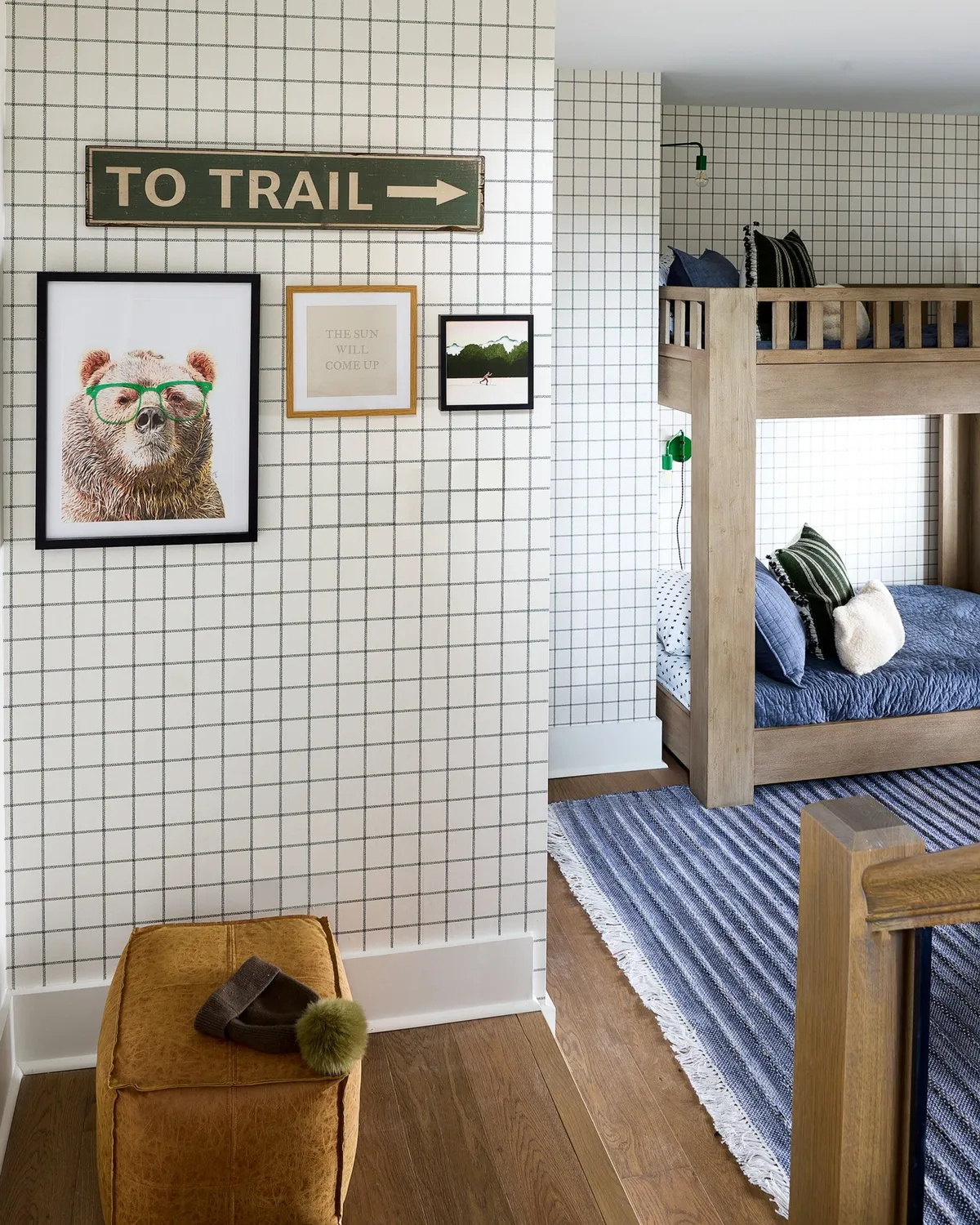 A whimsical bunk room featuring creative bear artwork, a 'to trail' sign, and cozy bunk beds with a striped rug and ottoman. The playful decor creates a welcoming space for children or friends, ideal for reading stories, playing games, or simply relaxing in a fun environment.