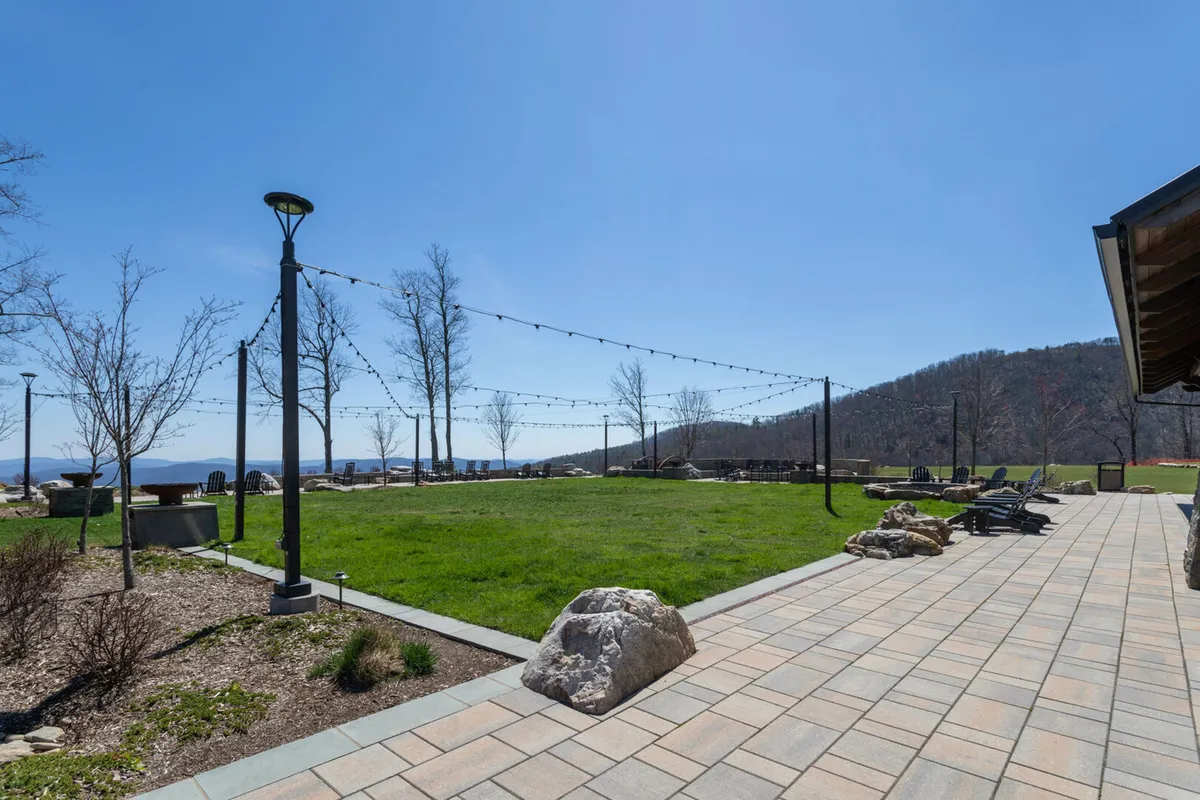 A cheerful communal lawn with string lights, a winding pathway, and panoramic mountain views. Residents relax in the seating area or gather for picnics, games, or summer events, bathed in the golden light of sunset.