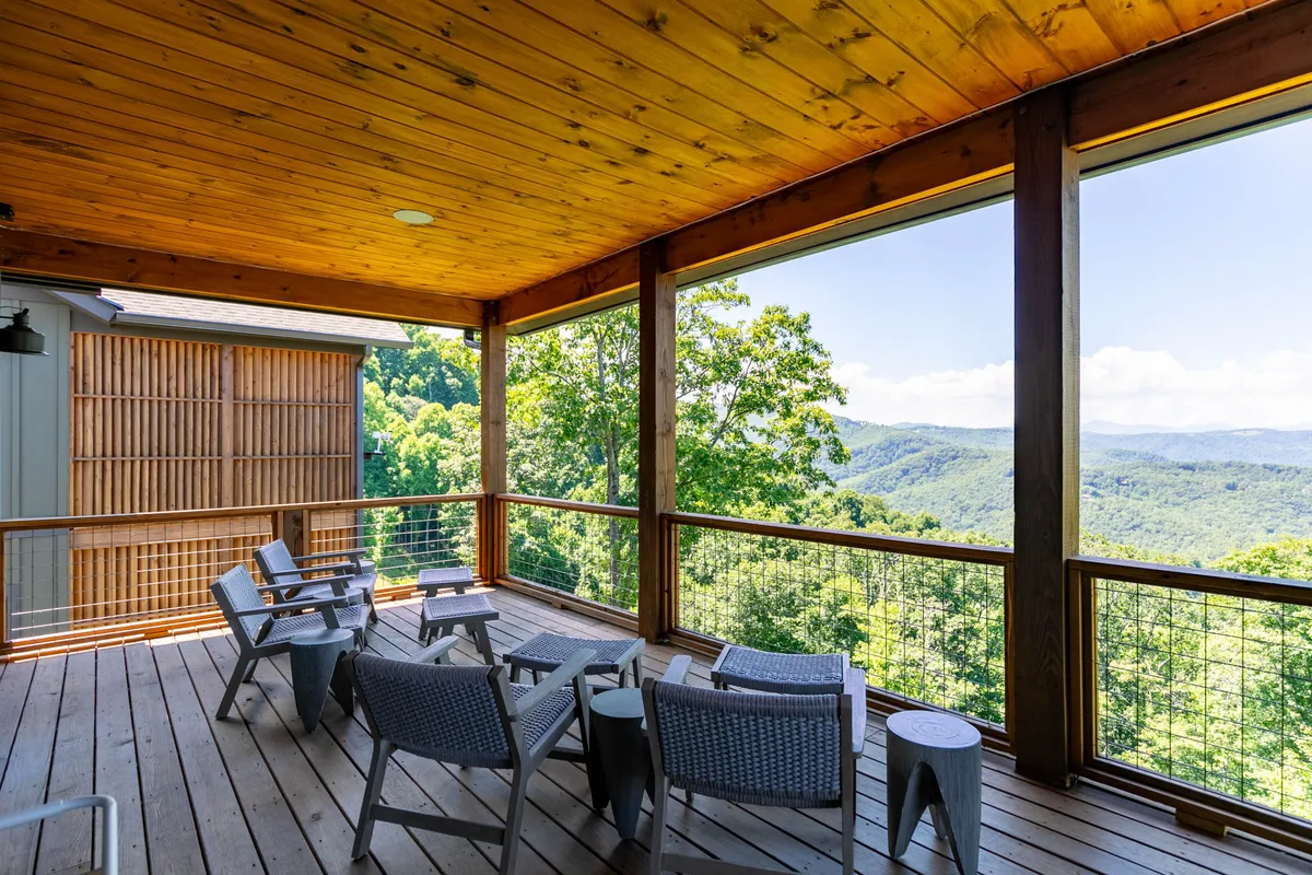 A serene, covered outdoor seating area with a mountain backdrop, inviting guests to lounge or practice morning yoga. The wooden deck and railings evoke an elevated mountain retreat feel, highlighting the tranquility and beauty of the natural setting.