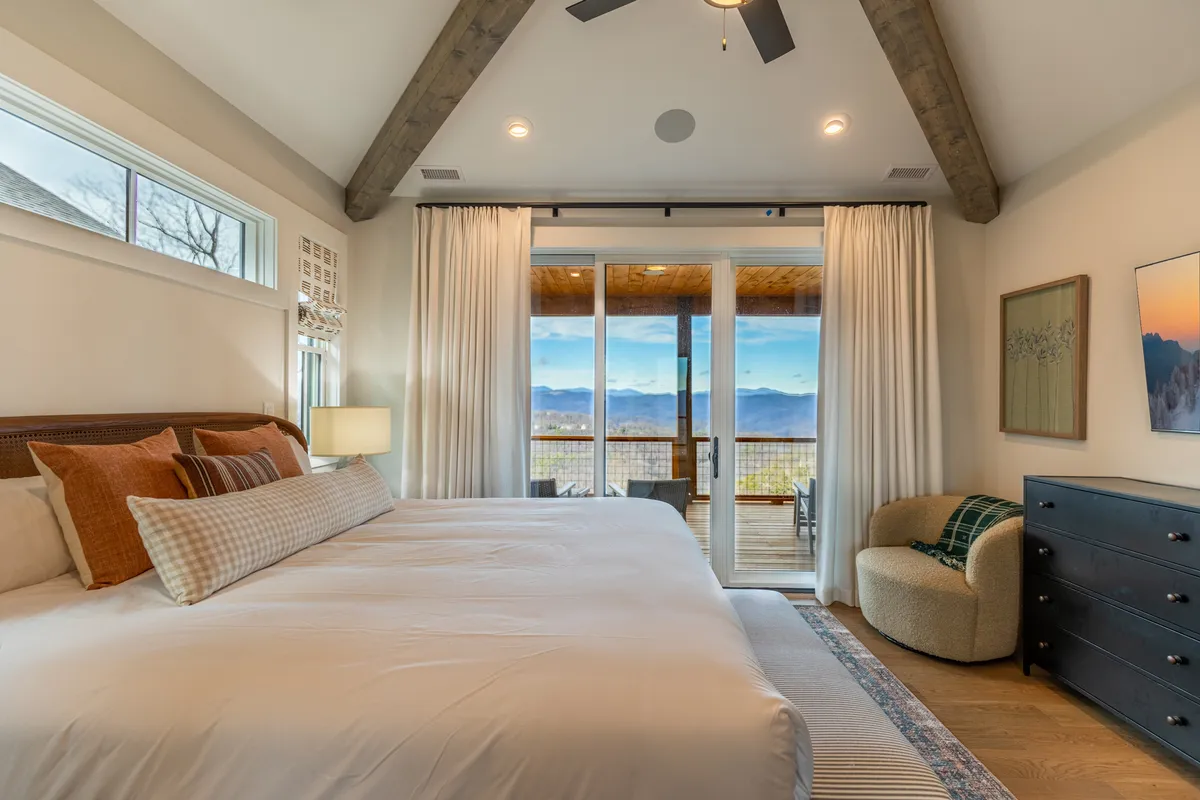 A spacious king-size bed is centered in the room, flanked by large windows that reveal breathtaking mountain views and flood the space with natural light. Decorative pillows and a cozy armchair create an inviting atmosphere for relaxation or reading. The serene mood is enhanced by soft neutral tones and subtle decor, making it a luxurious retreat for adults.