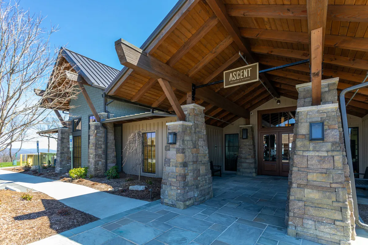 This exterior image features impressive stone pillars, sturdy wooden beams, and the community's entrance sign. The setting is tranquil and inviting, with a wide view that hints at the exclusivity and grandeur of the gated community beyond. Natural surroundings and architectural elements convey a sense of arrival, privacy, and security.