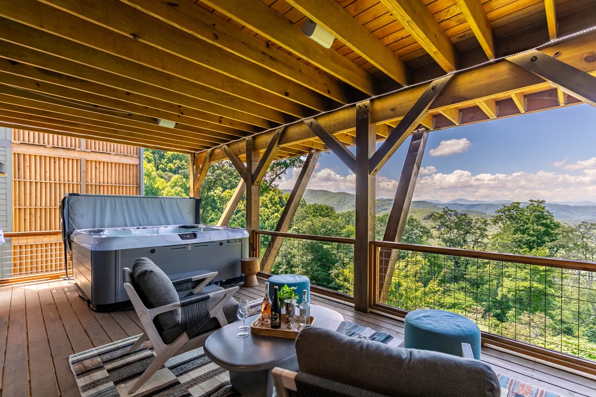 An inviting hot tub and seating area on a deck with sweeping views of the mountains. The setting sun paints the sky, creating a tranquil atmosphere ideal for unwinding, sharing stories, or stargazing with friends and family.