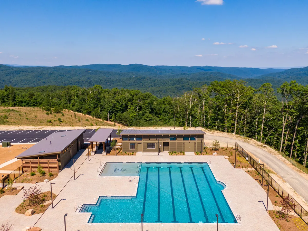 A spacious swimming pool surrounded by mountains, landscaped areas, and a modern community building. The pool area is designed for both relaxation and social events, with ample sunbathing space and gathering spots for community celebrations.