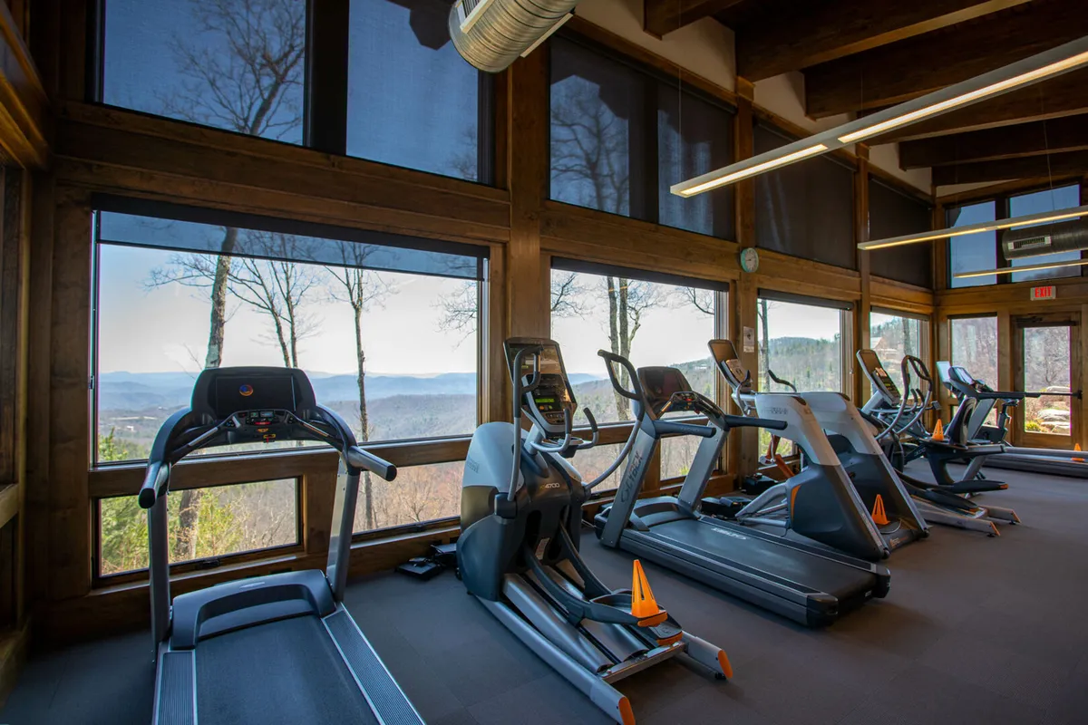 A modern fitness and wellness center with treadmills facing large windows that frame breathtaking mountain views. The natural light and scenic outlook create an invigorating atmosphere for year-round exercise, yoga, or meditation.